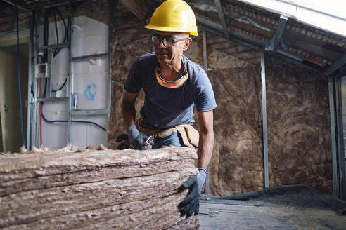 Älterer Bauarbeiter mit einem Stapel Isoliermaterial auf der Baustelle - ASGF04293
