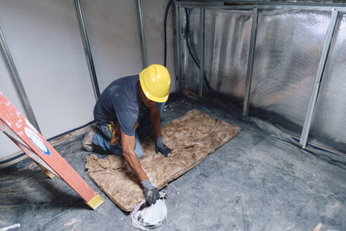 Construction worker working on insulation sheet at site - ASGF04296