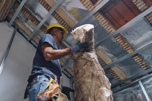 Construction worker working with insulation in attic - ASGF04299