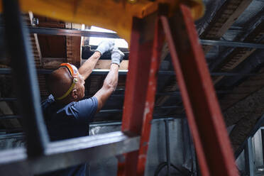 Bauarbeiter bei der Reparatur eines Deckenfensters im Dachgeschoss - ASGF04305