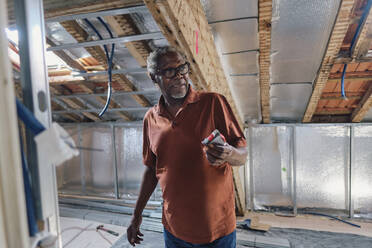 Senior man standing in attic at site - ASGF04309
