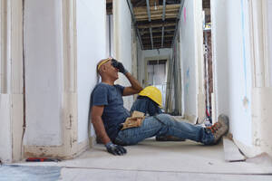 Glücklicher reifer Bauarbeiter, der seine Augen mit der Hand bedeckt und im Flur sitzt - ASGF04318