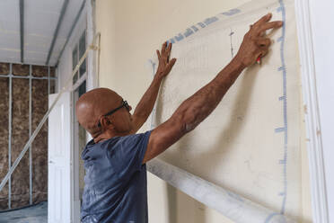 Älterer Bauarbeiter, der auf der Baustelle mit einem Maschendrahtgitter an der Wand misst - ASGF04336