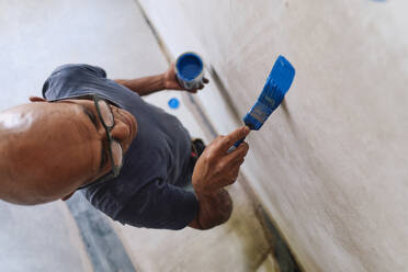 Bald construction worker applying blue paint on wall - ASGF04340