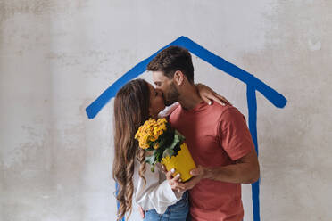 Paar, das sich küsst und einen Blumenstrauß vor einer Mauer auf einer Baustelle hält - ASGF04382