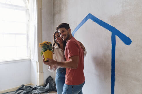 Glücklicher Mann und Frau mit Blumenstrauß vor einer Mauer auf einer Baustelle - ASGF04384