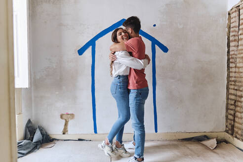 Happy couple hugging each other in front of wall at construction site - ASGF04385