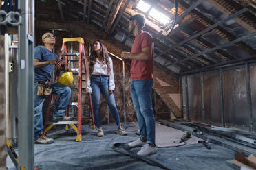 Man and woman having discussion with construction worker in attic at construction site - ASGF04395