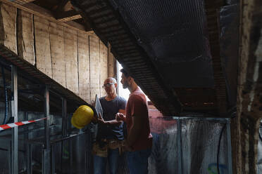 Bauarbeiter hält Solarpanel und diskutiert mit Mann auf dem Dachboden - ASGF04401