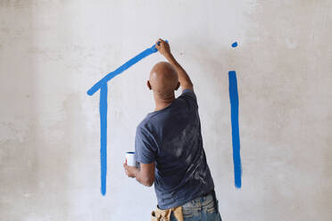 Bald construction worker drawing on wall with paintbrush at site - ASGF04409