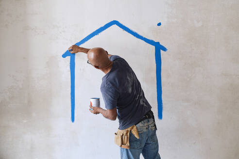 Bald construction worker drawing house on wall with paintbrush at site - ASGF04411