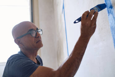 Bald construction worker wearing eyeglasses painting on wall - ASGF04413