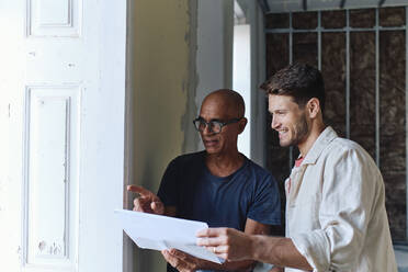 Happy architect discussing over document with man at site - ASGF04421