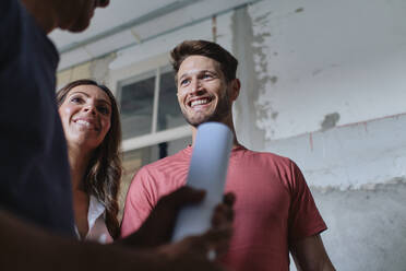 Happy man and woman discussing with construction worker at site - ASGF04428