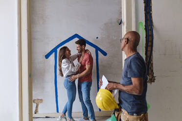 Construction worker with happy couple standing in front of wall at site - ASGF04435