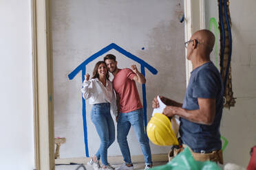 Construction worker with couple cheering in front of wall at site - ASGF04437