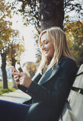 Lächelnde Frau mit Smartphone auf einer Bank sitzend - AZF00564