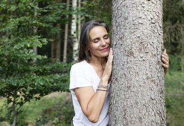 Lächelnde Frau, die einen Baum im Wald umarmt - JBYF00234