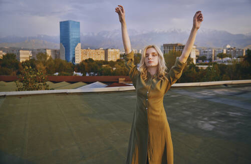 Carefree young woman with arms raised dancing on rooftop - AZF00566