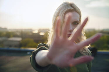 Ernste blonde Frau zeigt Stopp-Geste bei Sonnenuntergang - AZF00571