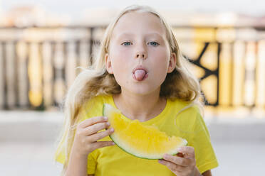 Mädchen hält ein Stück gelbe Wassermelone und zeigt die Zunge - SIF00801