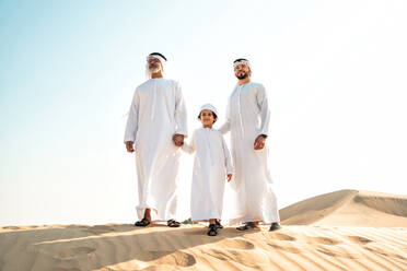 Drei-Generationen-Familie macht eine Safari in der Wüste von Dubai in weißer Kandura-Kleidung. Großvater, Sohn und Enkel verbringen Zeit zusammen in der Natur. - DMDF02621