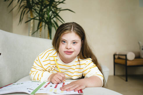 Mädchen mit Down-Syndrom macht Hausaufgaben im Wohnzimmer - MDOF01420