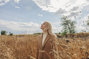 Blonde Frau steht mit geschlossenen Augen in einem Feld - VSNF01291