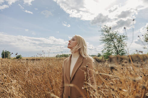 Blond woman standing with eyes closed in field - VSNF01291