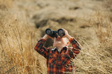 Boy looking through binoculars in wheat field - VSNF01296