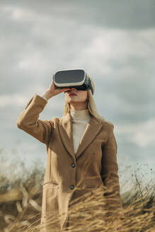 Blonde Frau trägt Virtual-Reality-Simulatoren unter bewölktem Himmel - VSNF01303