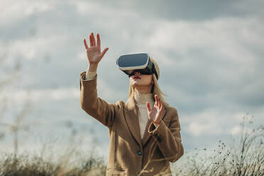 Woman gesturing with virtual reality simulators under cloudy sky - VSNF01304