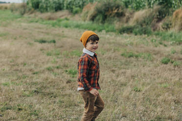 Happy boy wearing knit hat walking in field - VSNF01305