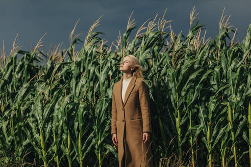 Blond woman standing with eyes closed in front of corn crops - VSNF01309