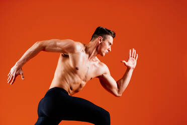 Athletic man with fit muscular body training in studio - Active man doing a workout, colorful lighting and background, concepts about fitness, sport and health lifestyle - DMDF02629