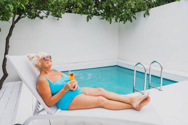 Glückliche ältere Frau mit Party im Schwimmbad - Schöne ältere Dame Sonnenbaden und Entspannen in einem privaten Pool während der Sommerzeit - DMDF02640