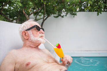 Glücklicher älterer Mann mit Party im Schwimmbad - Aktive ältere männliche Person beim Sonnenbaden und Entspannen in einem privaten Pool im Sommer - DMDF02648