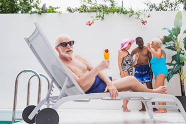 Glücklicher älterer Mann mit Party im Schwimmbad - Aktive ältere männliche Person beim Sonnenbaden und Entspannen in einem privaten Pool im Sommer - DMDF02652