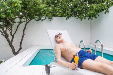 Happy senior man having party in the swimming pool - Active elderly male person sunbathing and relaxing in a private pool during summertime - DMDF02653