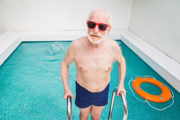 Happy senior man having party in the swimming pool - Active elderly male person sunbathing and relaxing in a private pool during summertime - DMDF02679