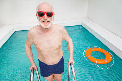 Happy senior man having party in the swimming pool - Active elderly male person sunbathing and relaxing in a private pool during summertime - DMDF02680