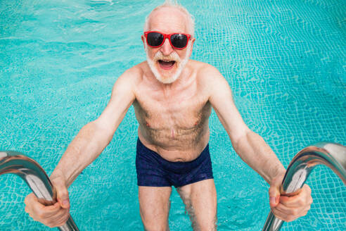 Happy senior man having party in the swimming pool - Active elderly male person sunbathing and relaxing in a private pool during summertime - DMDF02682