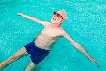 Happy senior man having party in the swimming pool - Active elderly male person sunbathing and relaxing in a private pool during summertime - DMDF02683