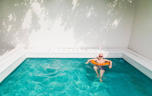 Happy senior man having party in the swimming pool - Active elderly male person sunbathing and relaxing in a private pool during summertime - DMDF02684