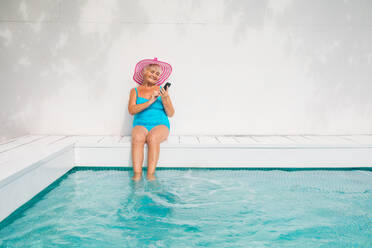 Happy senior woman having party in the swimming pool - Beautiful senior lady sunbathing and relaxing in a private pool during summertime - DMDF02695