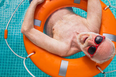 Happy senior man having party in the swimming pool - Active elderly male person sunbathing and relaxing in a private pool during summertime - DMDF02698