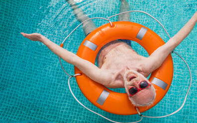 Happy senior man having party in the swimming pool - Active elderly male person sunbathing and relaxing in a private pool during summertime - DMDF02699