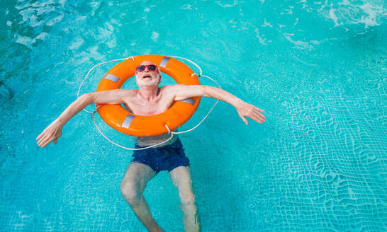 Happy senior man having party in the swimming pool - Active elderly male person sunbathing and relaxing in a private pool during summertime - DMDF02700