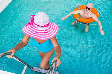 Happy senior couple having party in the swimming pool - Elderly friends releaxing at a pool party during summer vacation - DMDF02701