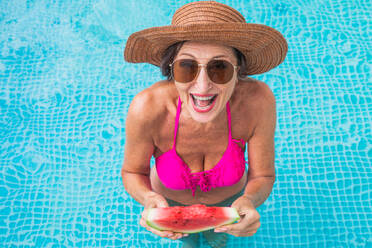 Glückliche ältere Frau mit Party im Schwimmbad - Schöne ältere Dame Sonnenbaden und Entspannen in einem privaten Pool während der Sommerzeit - DMDF02707